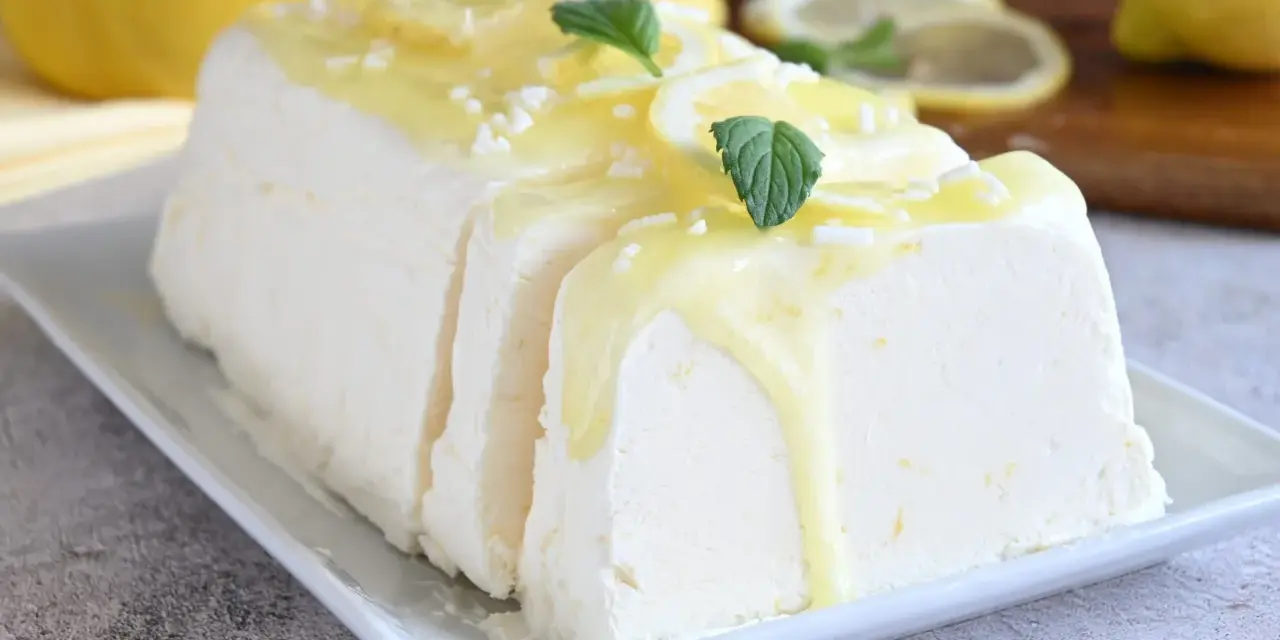 Un delizioso semifreddo al limone, guarnito con scorzette, menta e una glassa gialla brillante, pronto per essere gustato.
