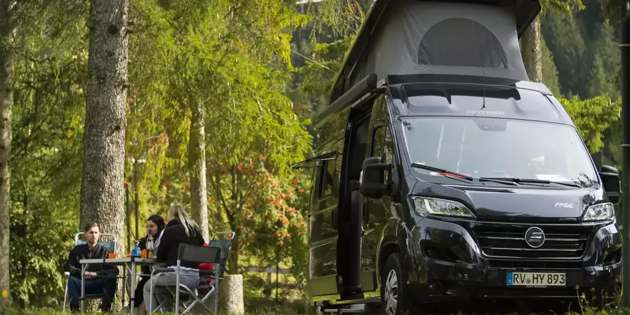 En solig dag med en clever sunny 540 husbil parkerad i skogen. Tre personer sitter vid ett bord och njuter av naturen.