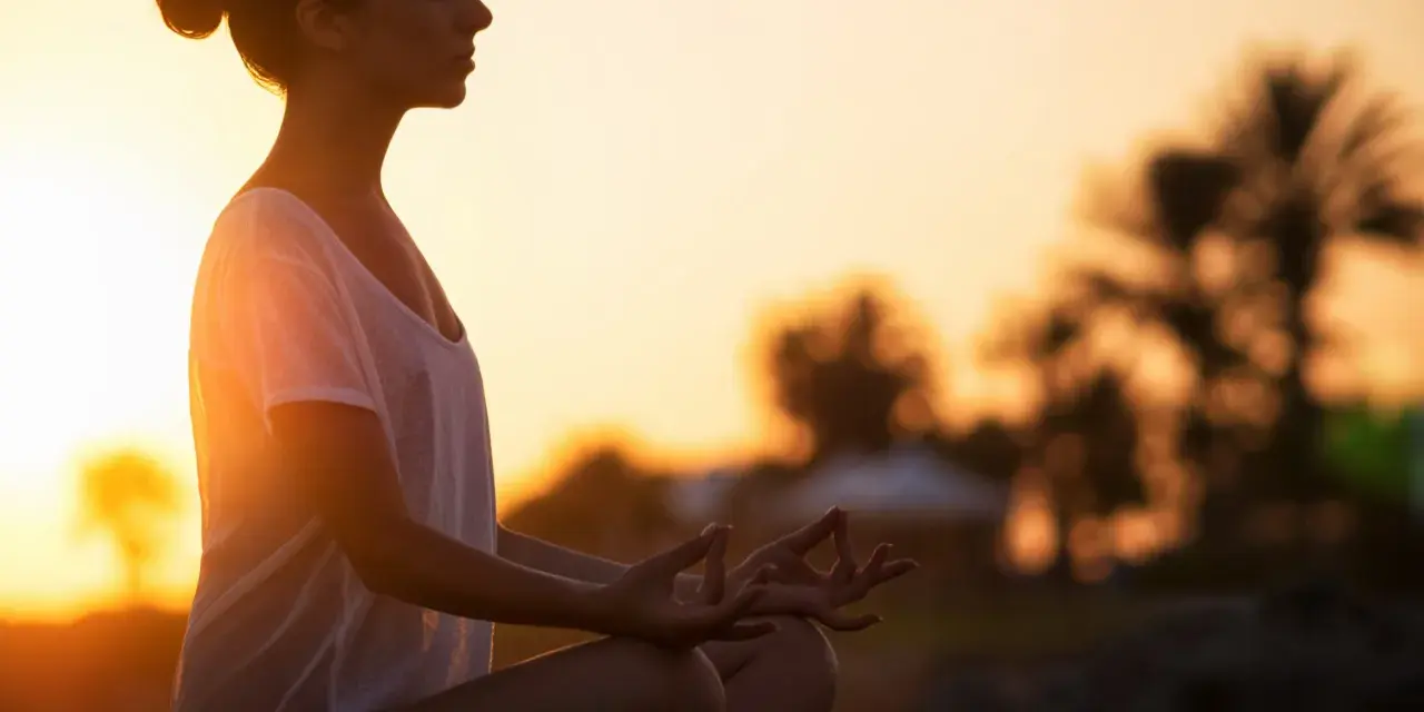 Frau meditiert im Sonnenuntergang. Ein kurzer 5-Minuten-Meditations-Text könnte hier perfekt passen, um diese friedliche Szene zu vertiefen.