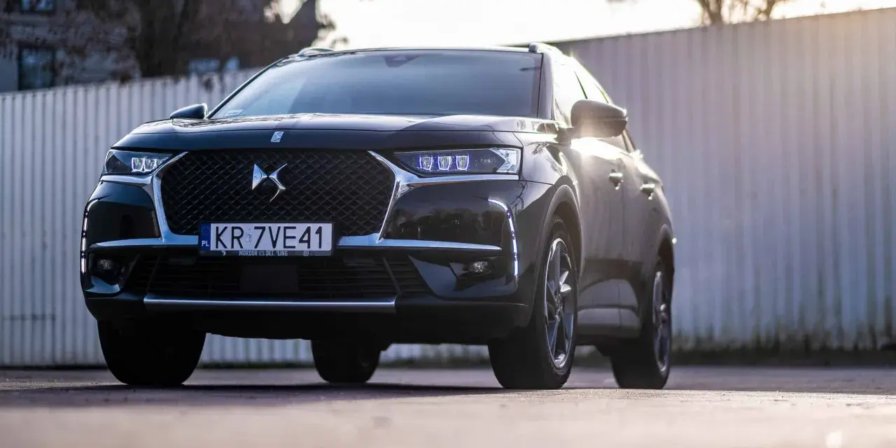 Czarny DS 7 Crossback z silnikiem 1.6 PureTech, z przodu, z niebieskimi światłami LED, na tle ogrodzenia.