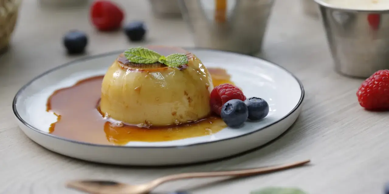 Delicioso flan de queso con caramelo, adornado con menta y frutos rojos.