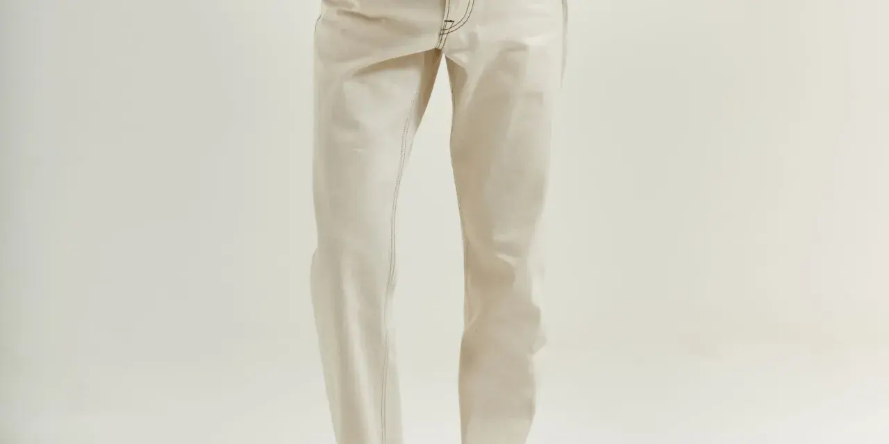 Uomo con giacca marrone e jeans chiari. La vestibilità è slim, non skinny, con risvolti alla caviglia.