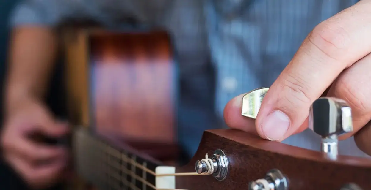 Dłoń stroi gitarę, kręcąc kluczem, by uzyskać idealny dźwięk E.