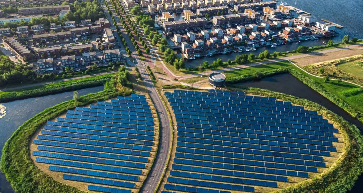 Un grande campo di pannelli solari, simbolo di rigenerazione urbana significato, circonda un quartiere residenziale con case moderne e canali.