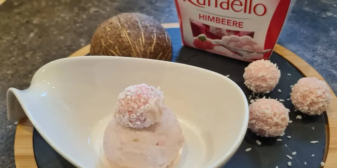 Ein Löffel Raffaello Himbeer Eis in einer Schale, daneben drei Raffaello-Kugeln und eine Kokosnuss.