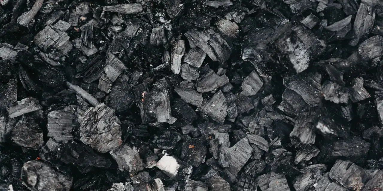 Gros plan sur des morceaux de machefer pellet, résidus noirs et gris de combustion, évoquant la chaleur d'un feu de bois.
