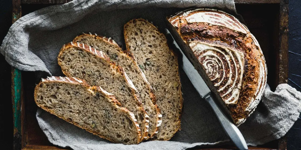 Ein rustikales Roggenbrot, in Scheiben geschnitten, liegt in einer Holzkiste auf Leinentuch. So vielseitig, was man aus Roggen machen kann!