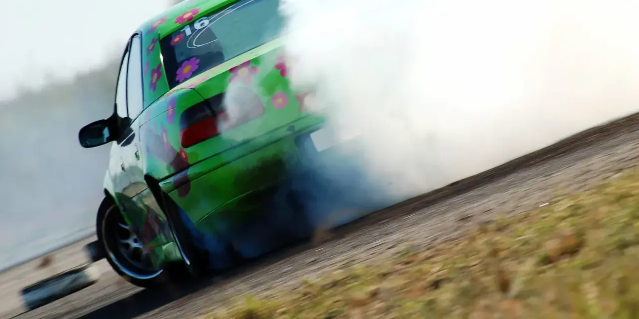 Zielony samochód z kwiatami driftuje, wydzielając dużo dymu.