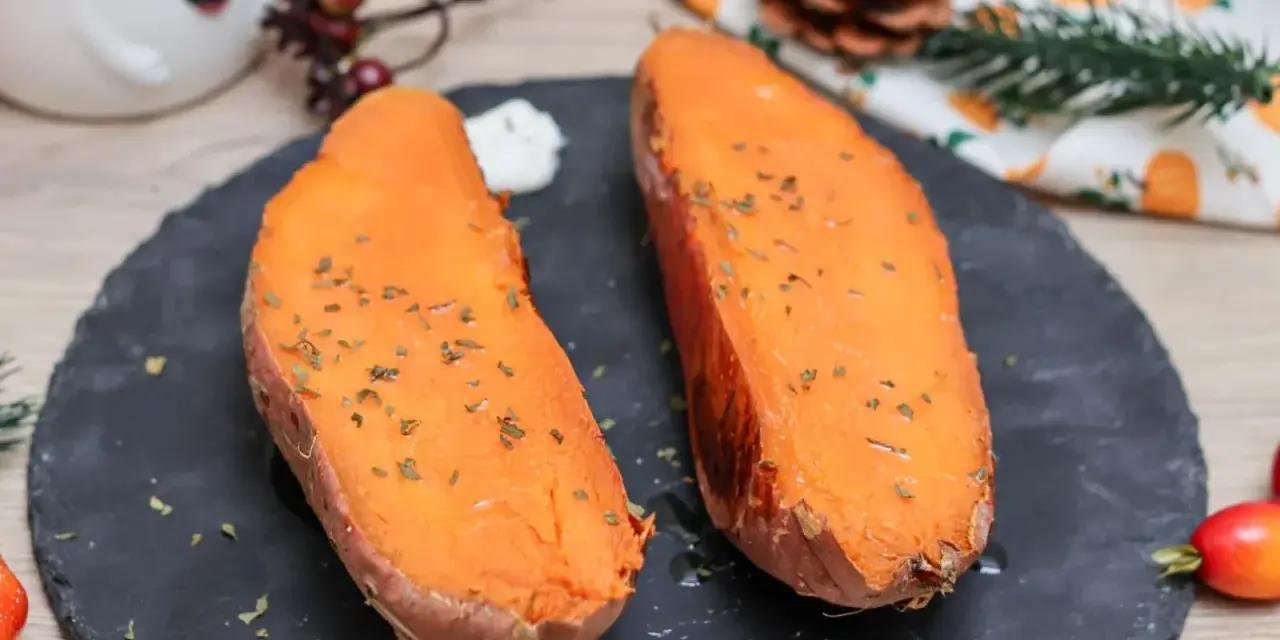 Dos mitades de boniato al horno, tiernas y doradas, con hierbas picadas y una cucharada de crema.