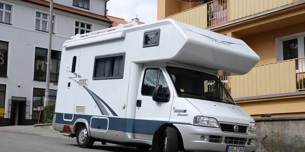 Biały kamper Fiat Ducato zaparkowany na ulicy. Zastanawiasz się, ile miejsc ma bus tego typu?