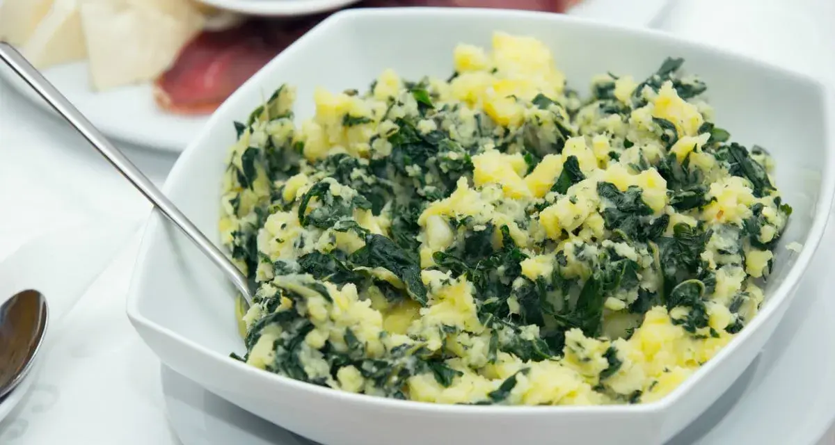 Un tazón blanco lleno de acelgas con patatas, un plato casero y reconfortante.