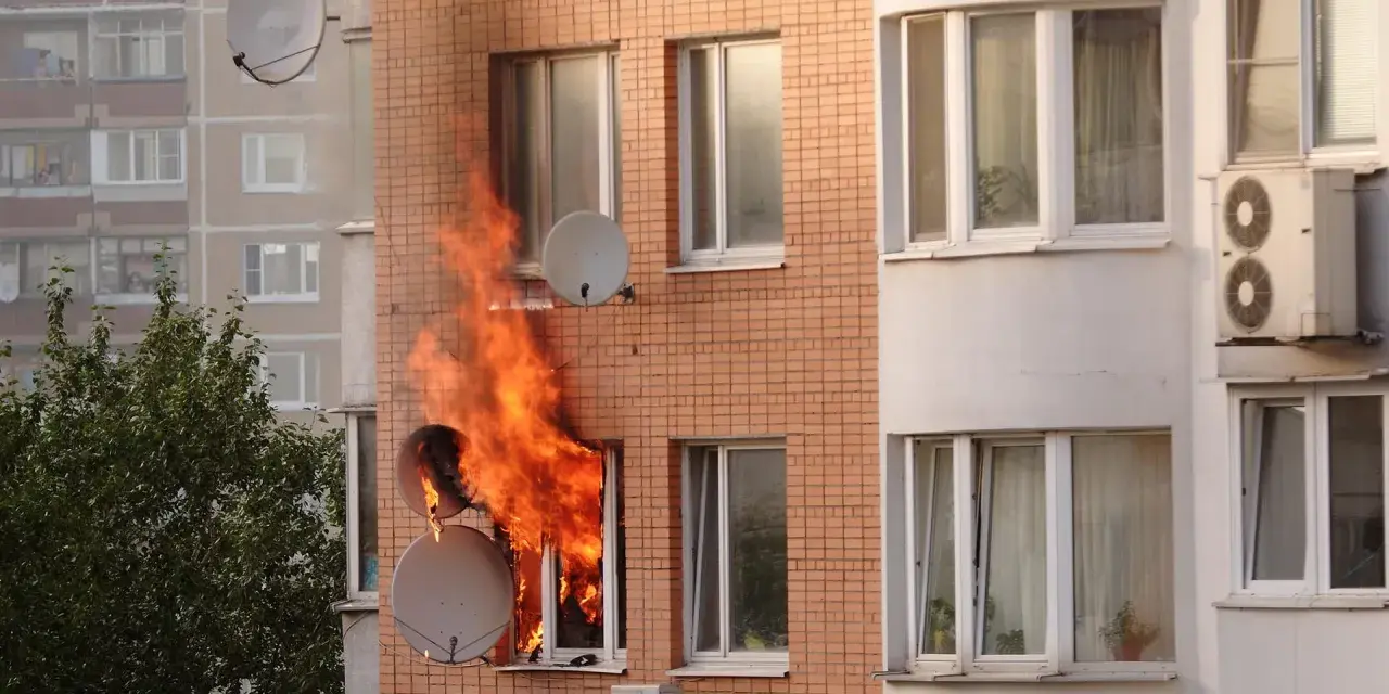 Flammen schlagen aus einem Fenster eines Mehrfamilienhauses. Ein trauriger Anblick, besonders wenn man bedenkt, dass es sich um einen wohnungsbrand ohne hausratversicherung handelt.