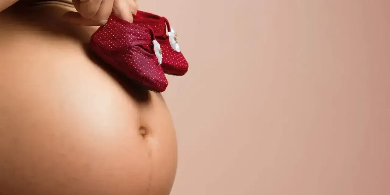 Brzuszek ciężarnej kobiety z małymi bucikami. Rozstępy to naturalna pamiątka po ciąży.