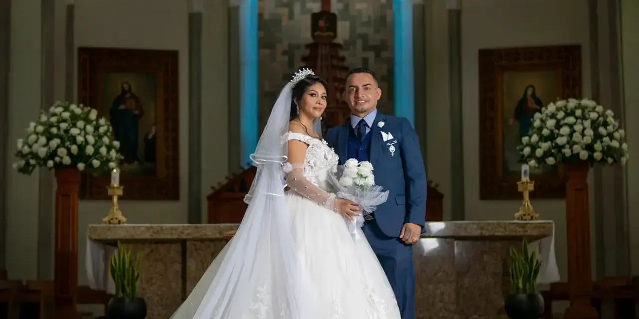 Para młoda w kościele. Zastanawiasz się, ile kosztuje ślub kościelny? Para wygląda na szczęśliwą, otoczona kwiatami i religijnymi obrazami.