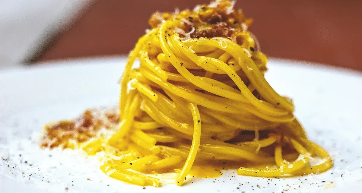 Un piatto di spaghetti alla carbonara fumante, guarnito con pecorino e pepe nero.