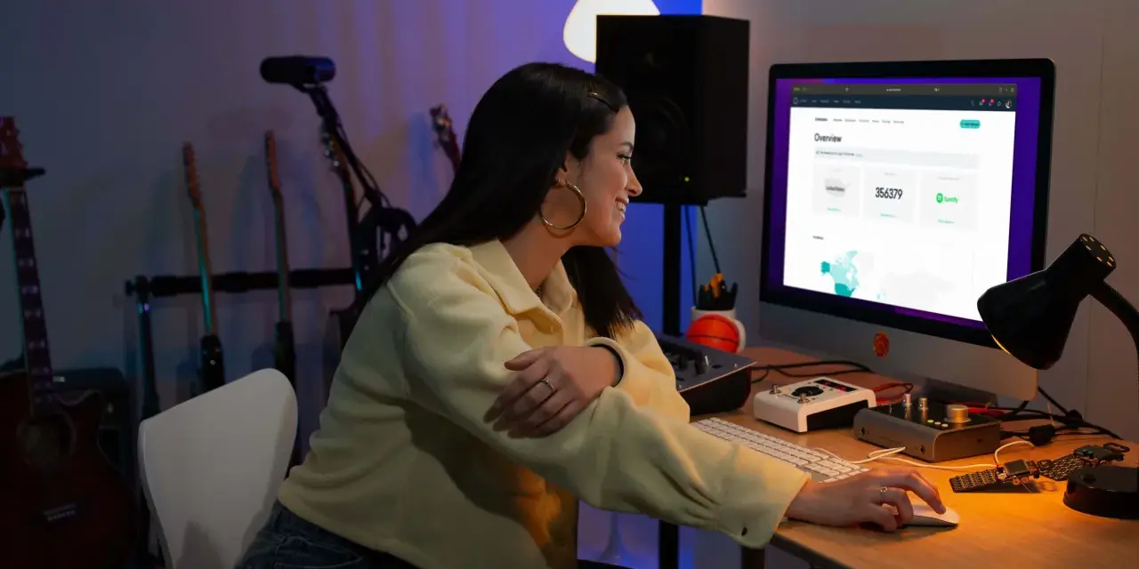 Junge Frau am Computer, die Statistiken für digitalen Musikvertrieb prüft. Gitarren im Hintergrund.