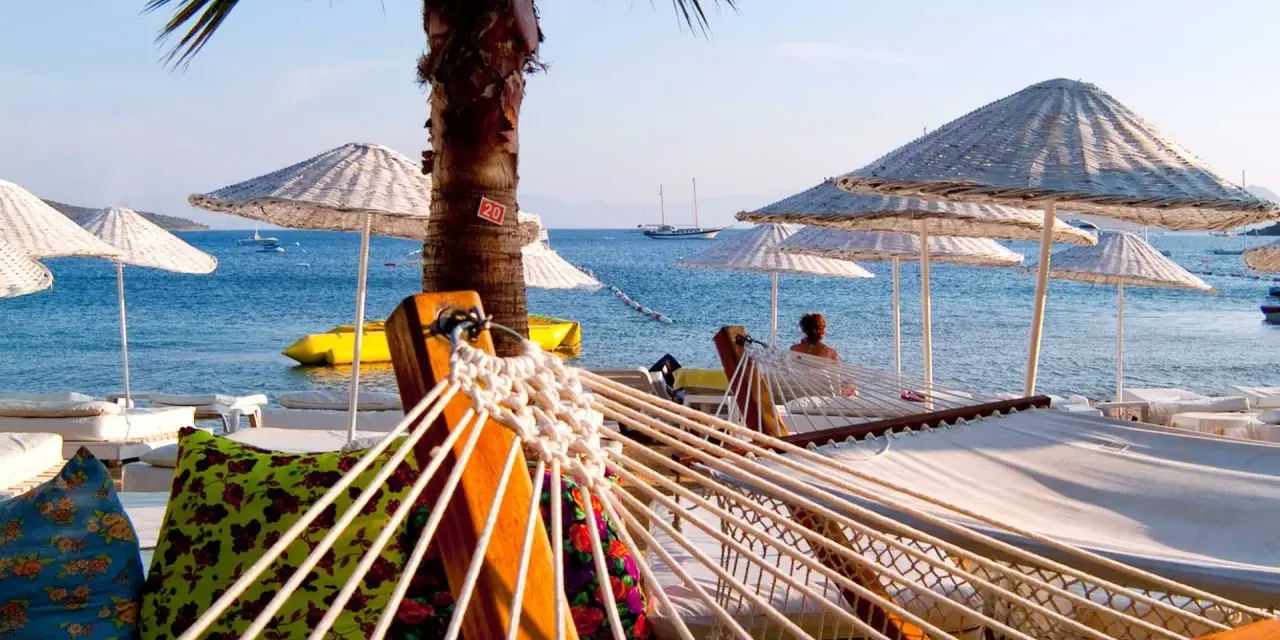 Hamaki i parasole na plaży w Turcji z widokiem na morze i żaglówki.