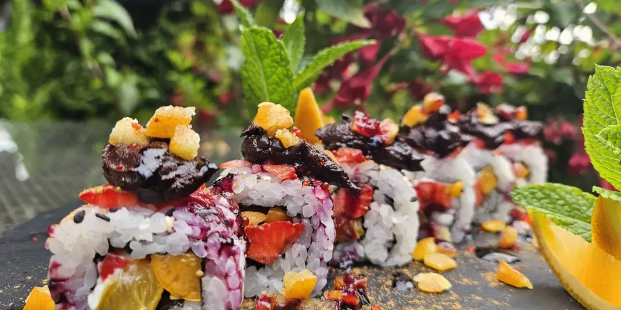 Roladki sushi z owocami, posypane cukrem pudrem i udekorowane miętą i pomarańczą.