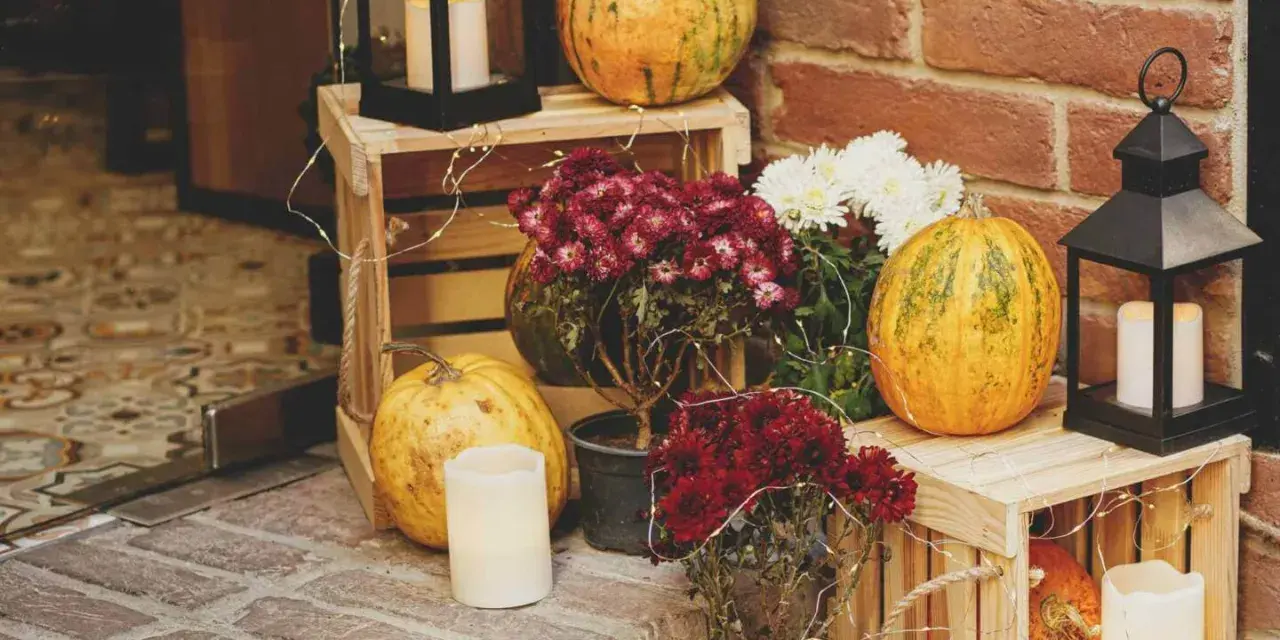 Gemütliche herbstdeko hauseingang mit Kürbissen, Laternen und Blumen auf Holzkisten.
