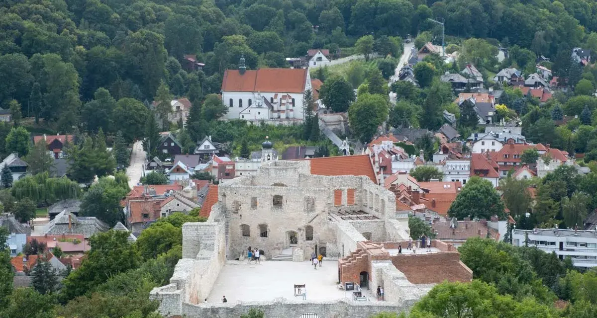 Ruiny zamku w Kazimierzu Dolnym na tle zielonych wzgórz i zabudowań.