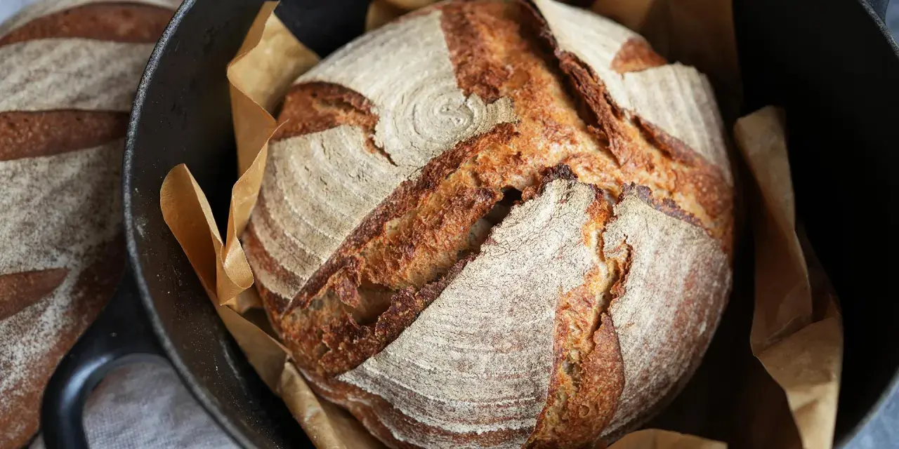 Ein frisch gebackenes Sauerteigbrot mit knuspriger Kruste liegt in einem Gusseisentopf. Perfekt für jedes Sauerteigbrot Rezept.