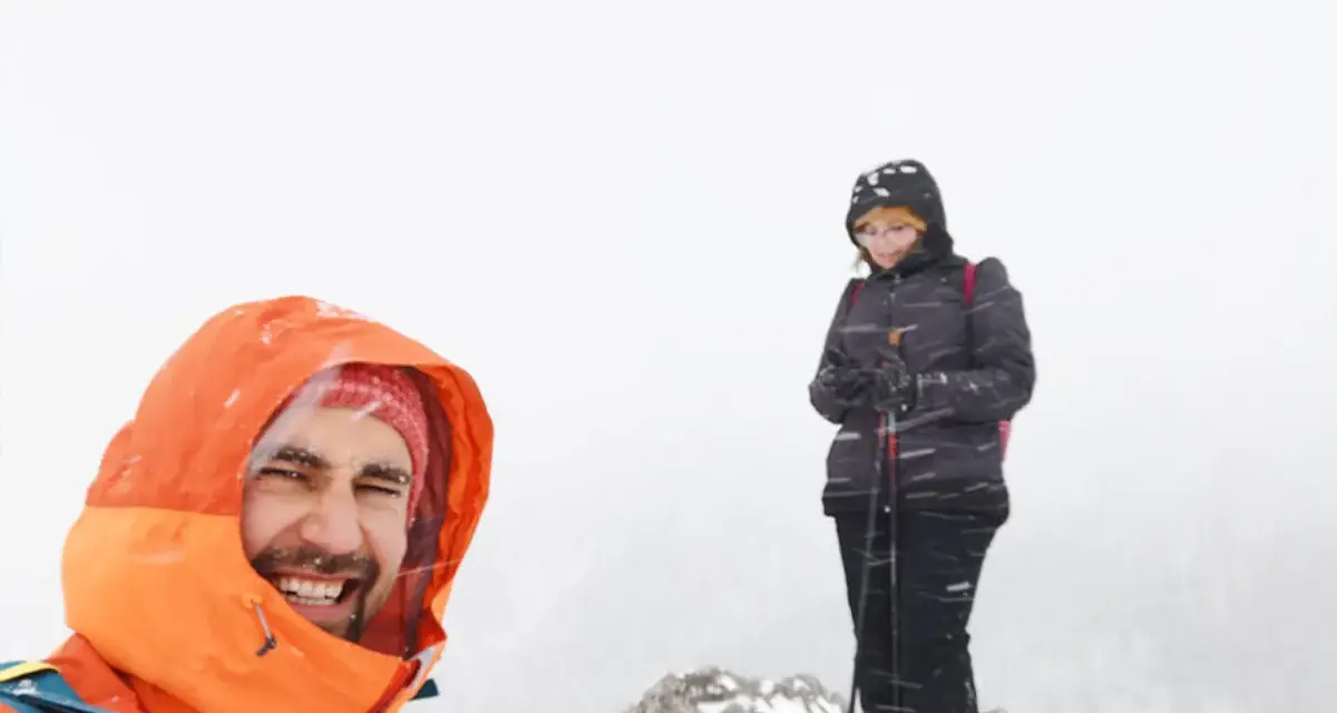 Uśmiechnięty turysta w pomarańczowej kurtce i kobieta z kijkami narciarskimi na tle mglistej doliny strążyskiej, blisko Sarniej Skały.