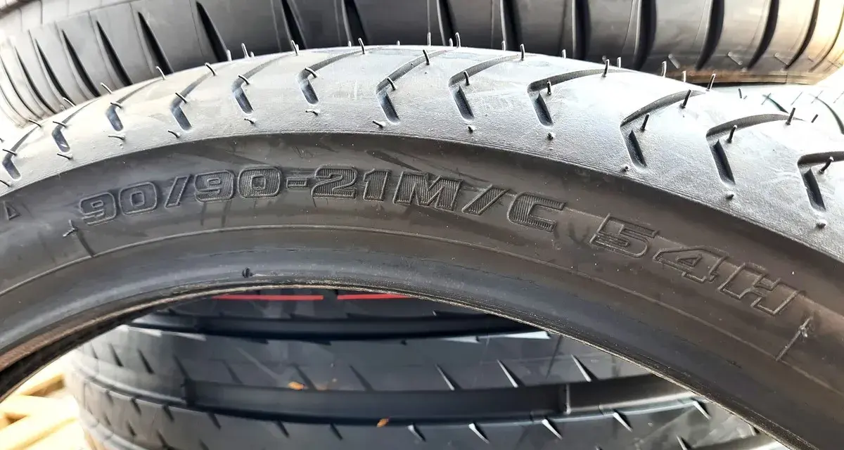Opona motocyklowa z oznaczeniem 90/90-21M/C 54H. Szerokość opony jest kluczowa dla przyczepności.