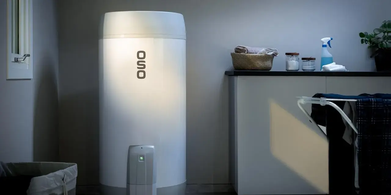 En OSO smart varmvattenberedare står i ett tvättstuga. Bredvid finns en tvättkorg och en torkställning med kläder.