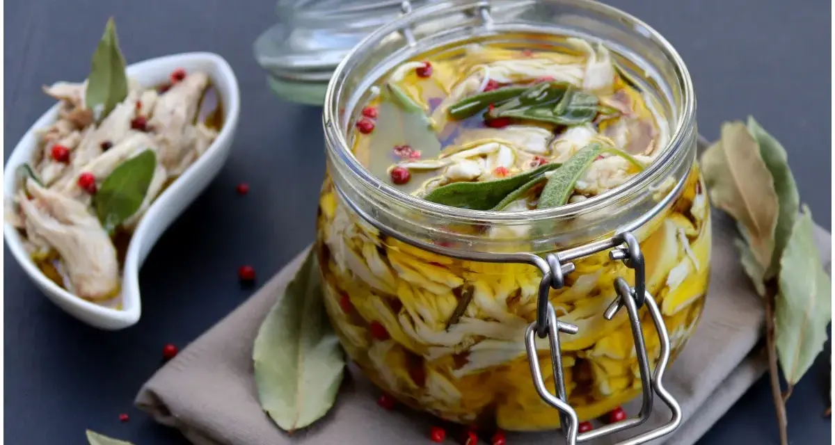 Tonno di coniglio sott'olio, sfilacciato e conservato in un barattolo di vetro con erbe aromatiche e pepe rosa.