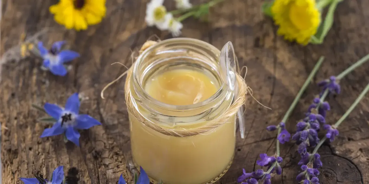 Vasetto di pappa reale, circondato da fiori blu e gialli. Chissà dopo quanto fa effetto questo prezioso nettare.