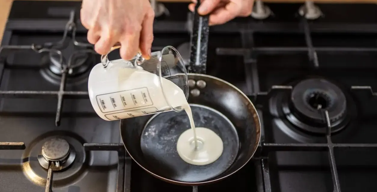 Mani versano panna da cucina in una padella su un fornello a gas.