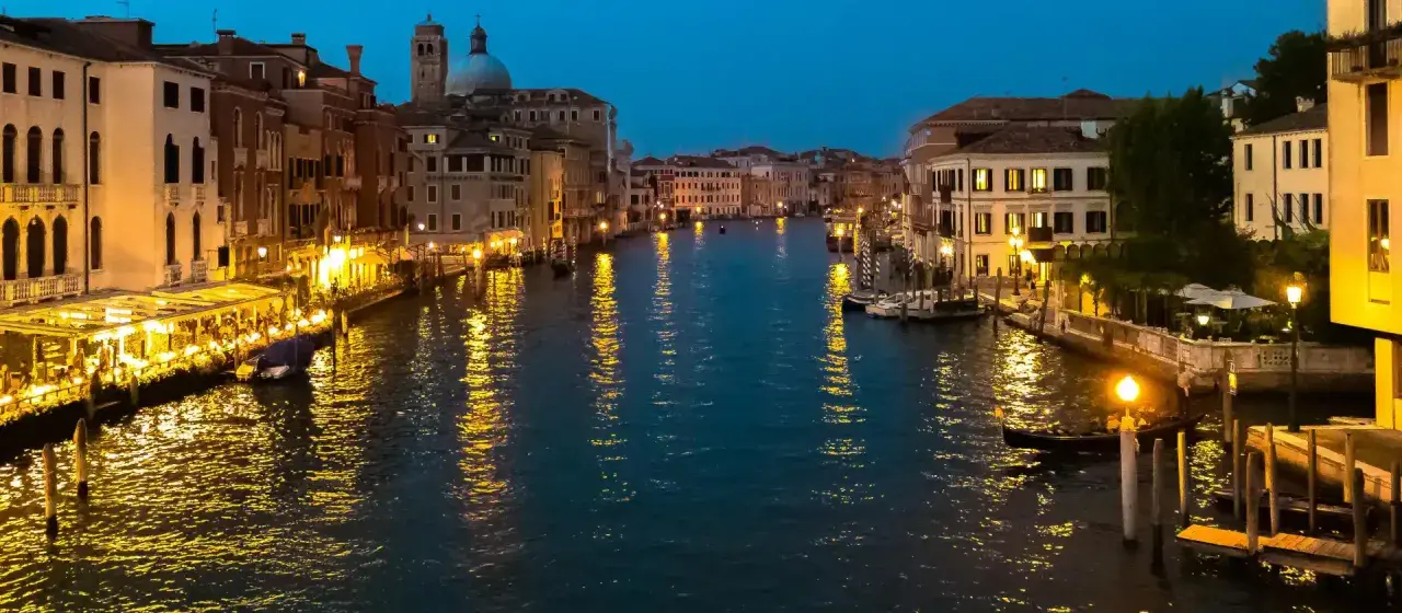 Serata magica per visitar Venezia: luci dorate sui palazzi e riflessi sull'acqua del Canal Grande, con gondole e ristoranti animati.