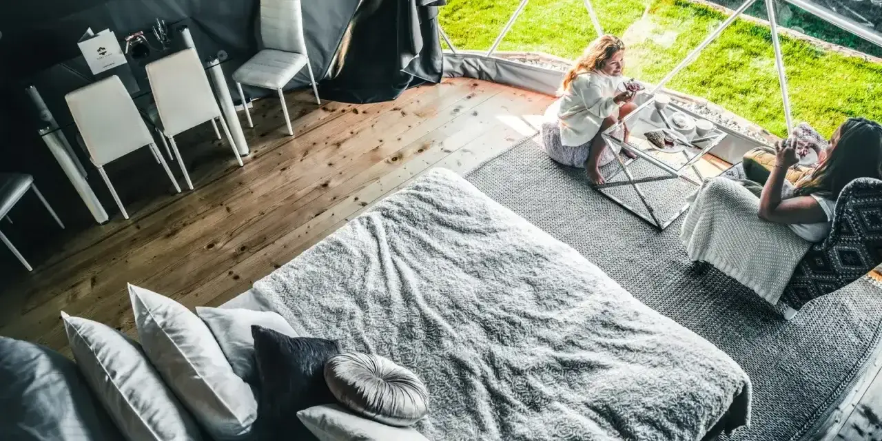 Dwie kobiety relaksują się w luksusowym namiocie. Przytulne wnętrze z wygodnym łóżkiem i stolikiem kawowym, idealne na camping w Zakopanem.