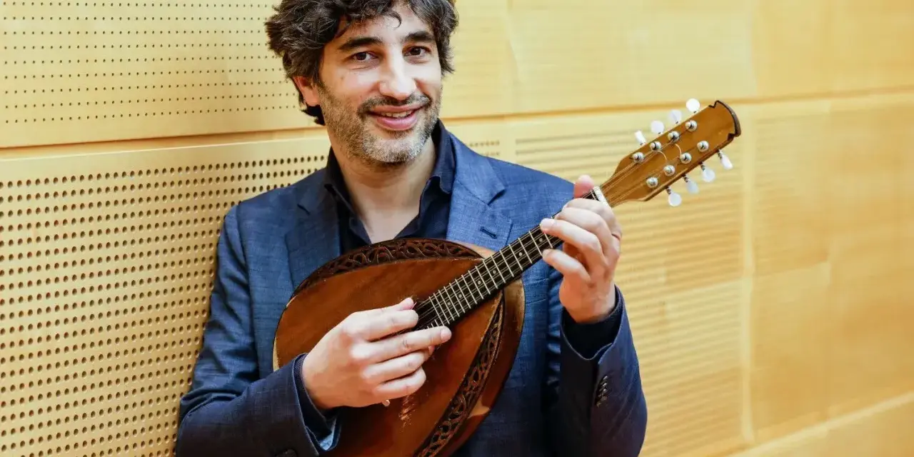 Mann mit Mandoline, die acht Saiten hat, lächelt.