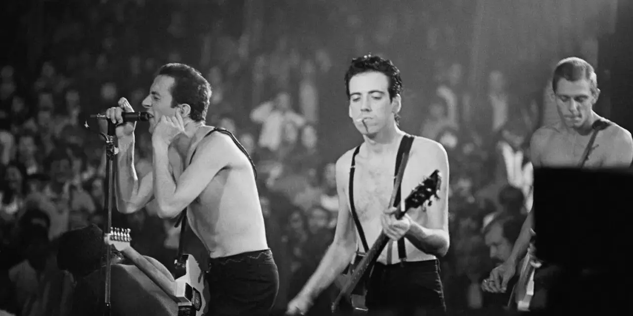 Le chanteur de The Clash, Joe Strummer, chante avec passion devant une foule en délire, guitare à la main.