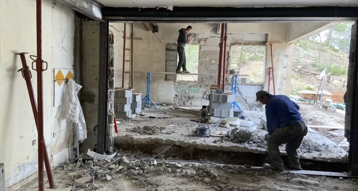 Travaux de démolition en cours pour une aide à la rénovation maison ancienne. Des ouvriers utilisent des outils pour casser le béton.