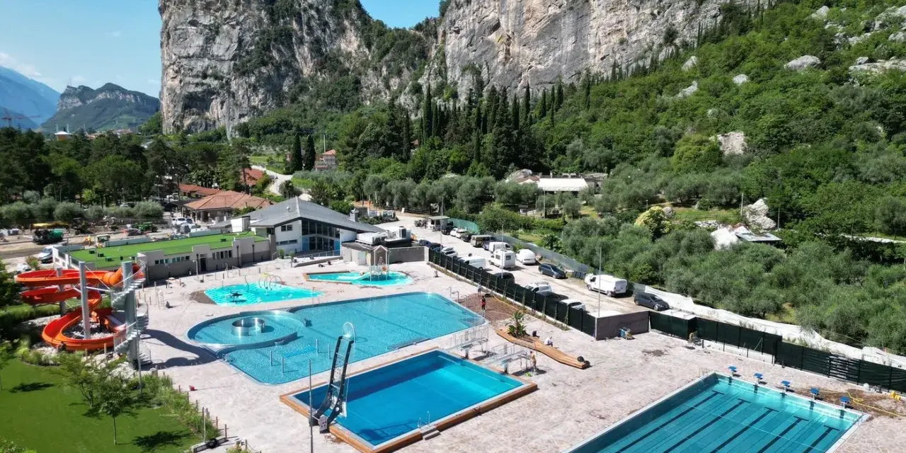 Kompleks basenów z atrakcjami wodnymi i zjeżdżalniami, otoczony zielenią i górami. Idealne miejsce na wakacje z rodziną, blisko natury, w okolicy **camping Arco**.