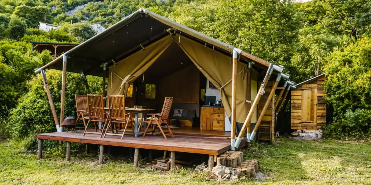Glamping w Czarnogórze: namiot z drewnianym tarasem, stołem i krzesłami, otoczony zielenią. Idealne miejsce na relaks.