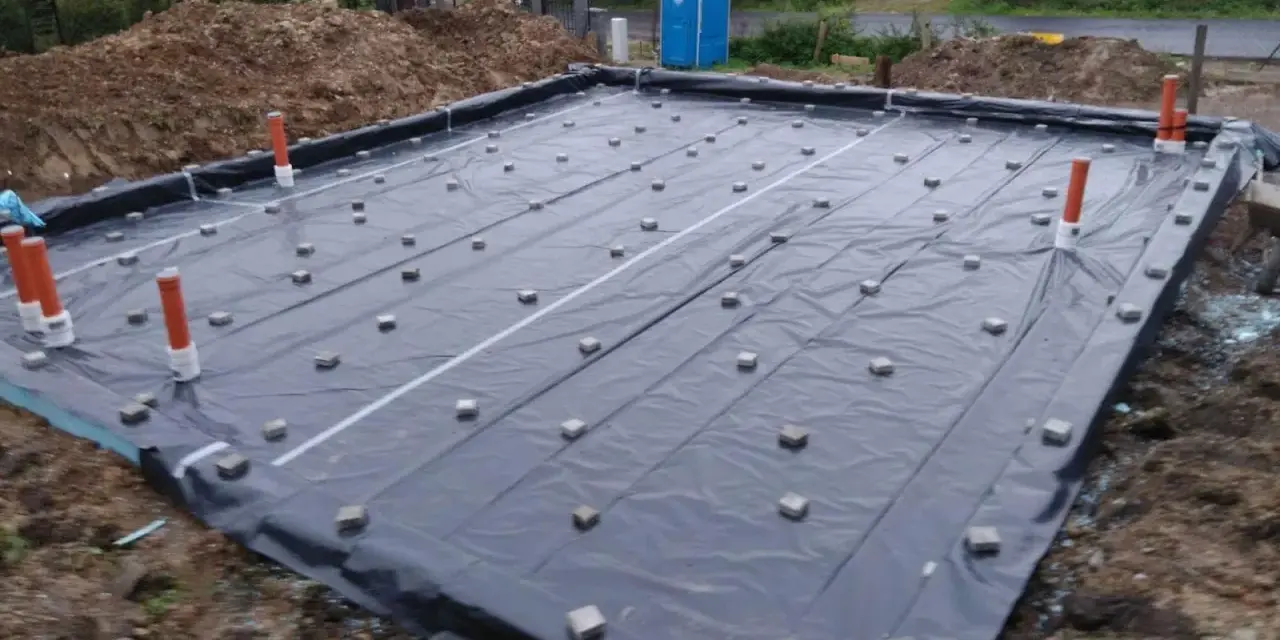 Fundament budowlany z folią i rurami. Widać małe kostki, które służą jako dystanse do zbrojenia, zapewniając odpowiednią grubość otuliny betonu.