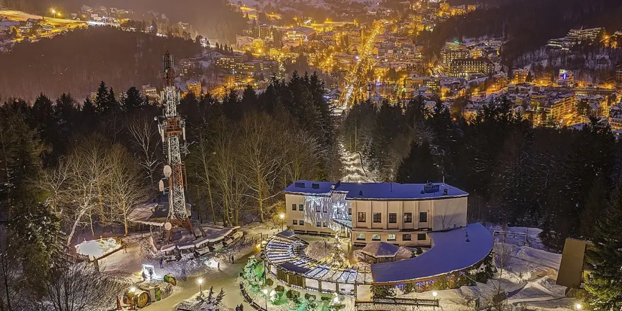 Wieczorna górska trasa pieszo w parku. Oświetlone miasto w dole, wieża telekomunikacyjna i budynek z iluminacjami.