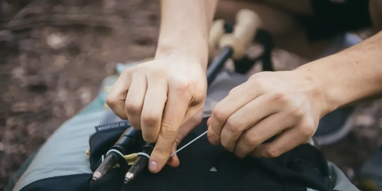 Ręce zapinają kijki trekkingowe do plecaka. Prosty sposób, jak przypiąć kijki do plecaka, by były zawsze pod ręką.