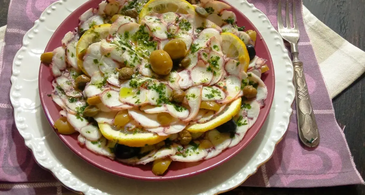 Carpaccio di polpo fresco, guarnito con olive, capperi e fette di limone, un piatto estivo da gustare.