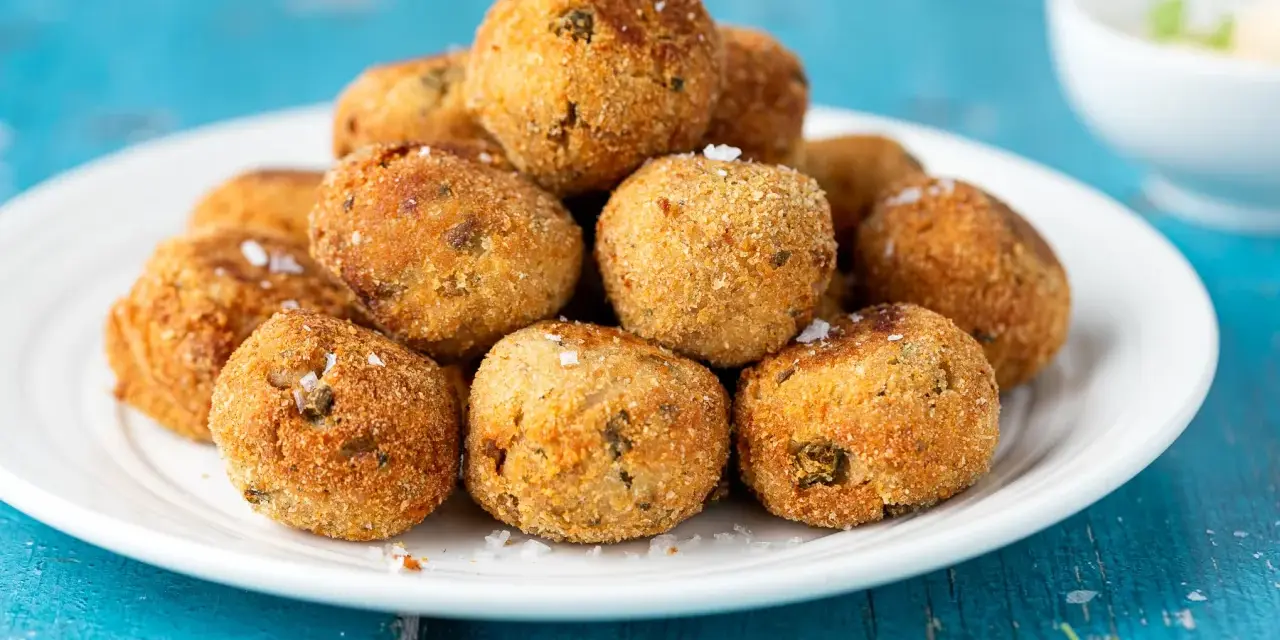 Pile di polpette tonno e ricotta dorate e croccanti, cosparse di sale grosso, su un piatto bianco.