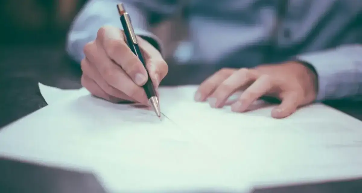 Dłoń pisze długopisem na papierze, finalizując wpis do księgi wieczystej.