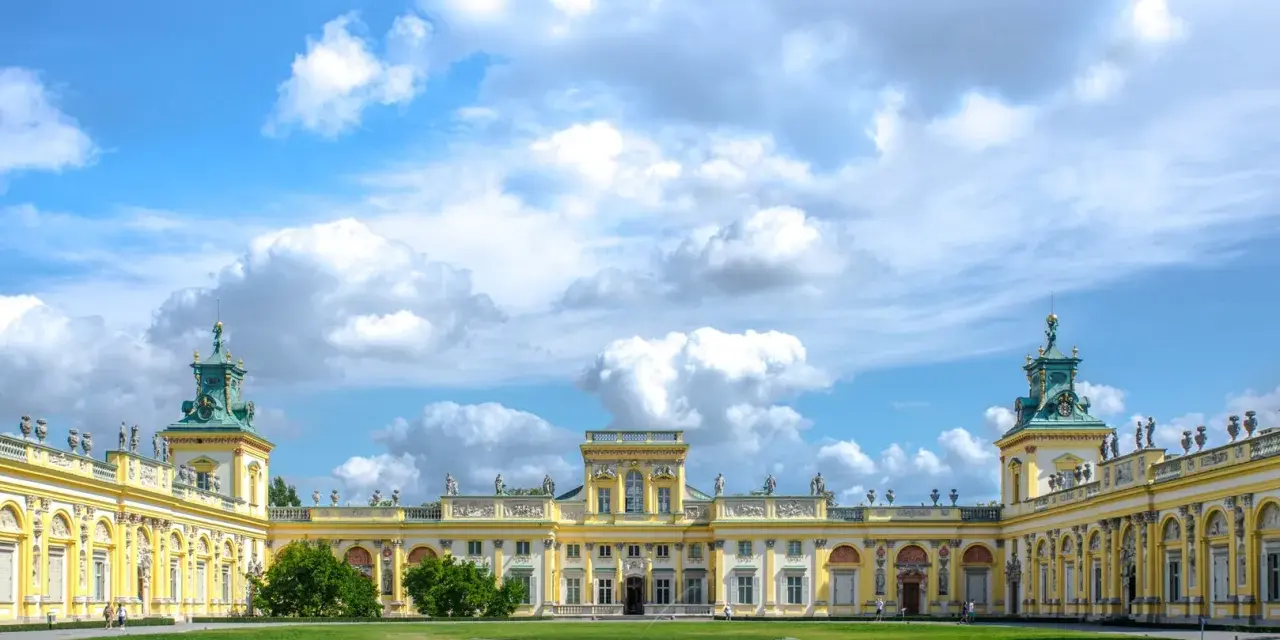 Pałac w Wilanowie zachwyca architekturą i ogrodami. Można zobaczyć bogato zdobione fasady, wieże i zielone trawniki.