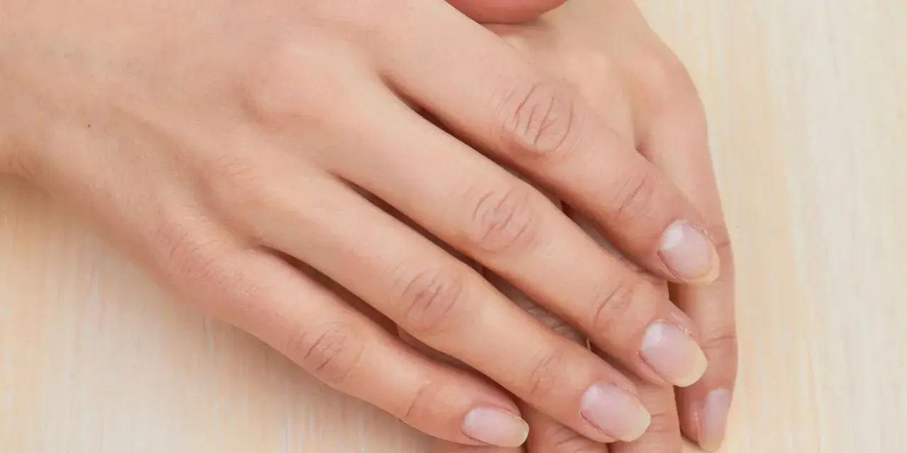Mani curate, con unghie naturali e sane che sembrano respirare. La pelle è liscia e luminosa, poggiata su una superficie chiara.