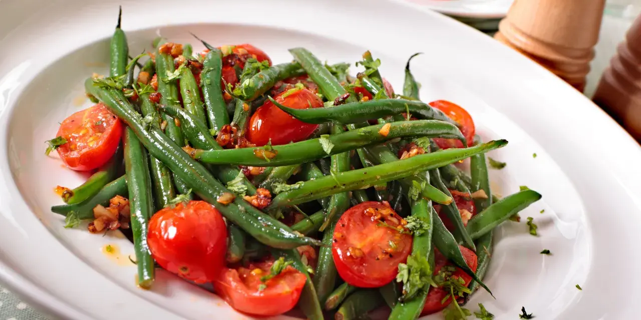 Insalata di fagiolini freschi con pomodorini ciliegino e erbe aromatiche, servita in un piatto bianco.