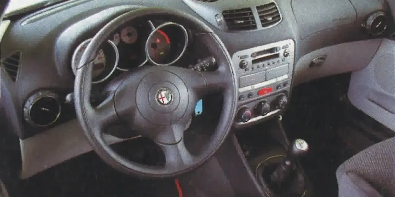 Wnętrze Alfa Romeo 147 1.9 JTD: kierownica, deska rozdzielcza z radiem i nawiewami, dźwignia zmiany biegów.