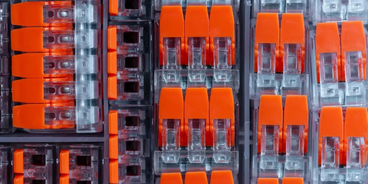 Zbliżenie na pomarańczowe złącza elektryczne w przezroczystych obudowach, ułożone w rzędy.