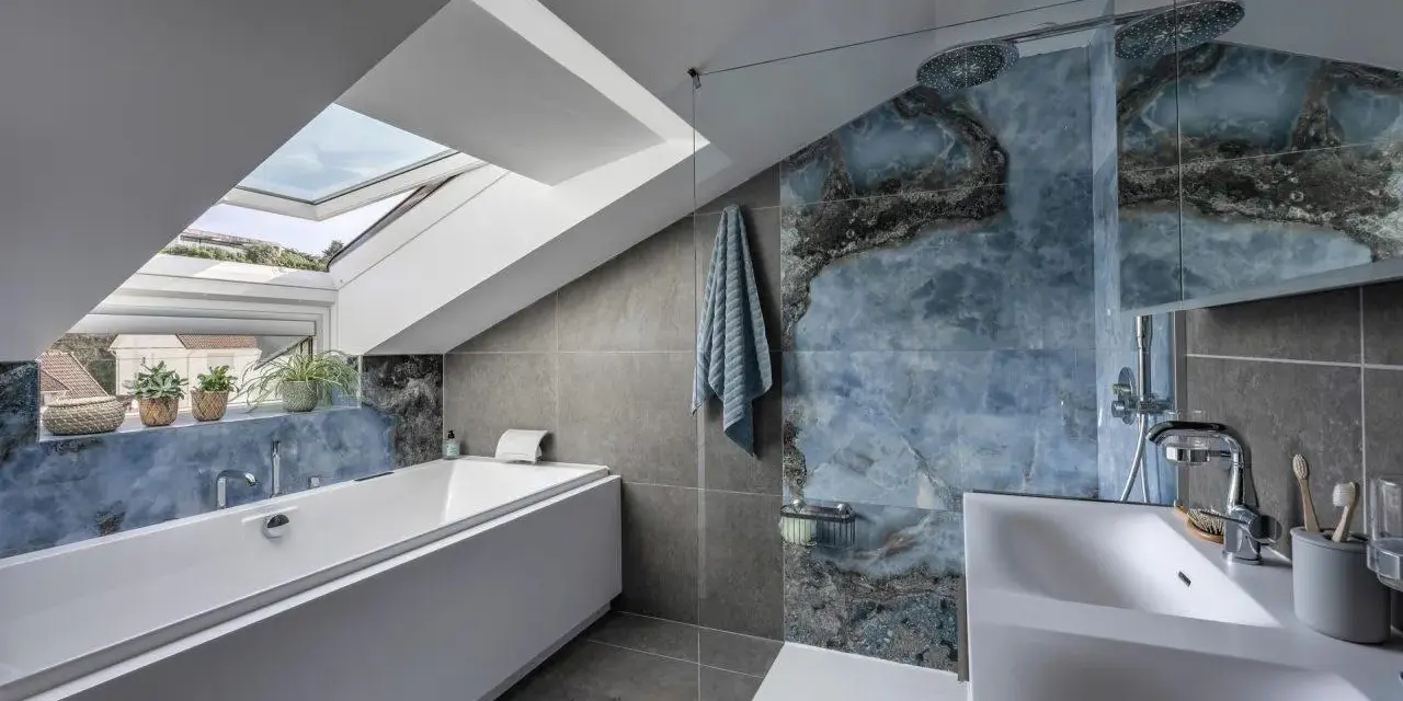 Bagno sottotetto basso con vasca, doccia con piastrelle blu marmorizzate e lucernario.
